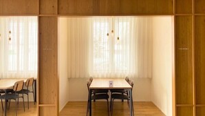 A dining area with a wooden table and chairs, a window with sheer curtains, and a wooden partition. - Bibai ekimae hotel BIJIKO (Bibai)