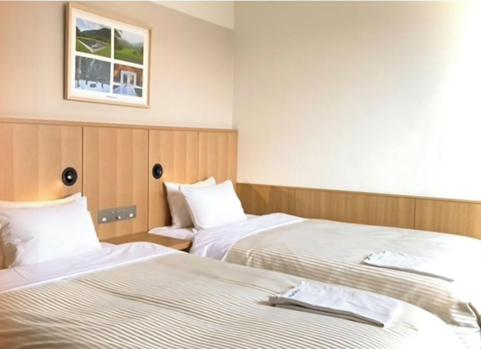 Een hotelkamer met twee bedden, een houten hoofdbord, een ingelijst schilderij aan de muur en een nachtkastje.