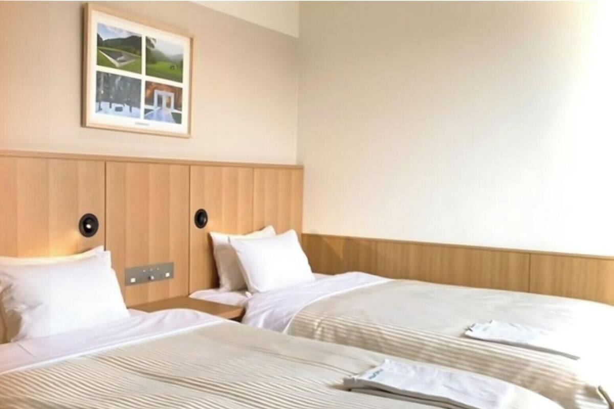 A hotel room with two beds, a wooden headboard, a framed picture on the wall, and a bedside table.