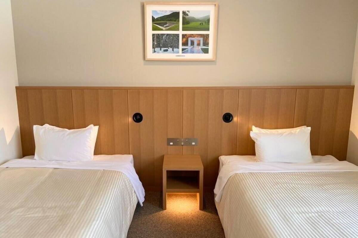 A hotel room with two beds, a wooden headboard, a small bedside table, and a framed picture on the wall.
