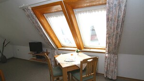 A dining area with a table and chairs, a television on a stand, and a window with curtains. - House Gräpel App. 5, Germany (Hörnum (Sylt))
