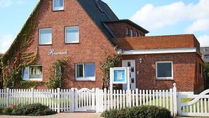 Een bakstenen gebouw met een witte picket hek, een bord met de tekst 'Roseneck' en een kleine tuin aan de voorzijde.