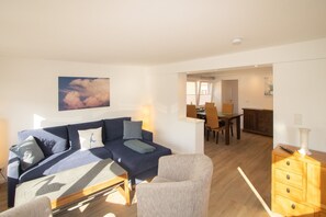 Ein Wohnzimmer mit einer Couch, Sesseln, einem Holzkabinett und einem Essbereich mit Stühlen und einem Tisch.