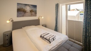 Un dormitorio con cama, lámparas de noche, ventana con cortinas, un cuadro en la pared y una mesita de noche.