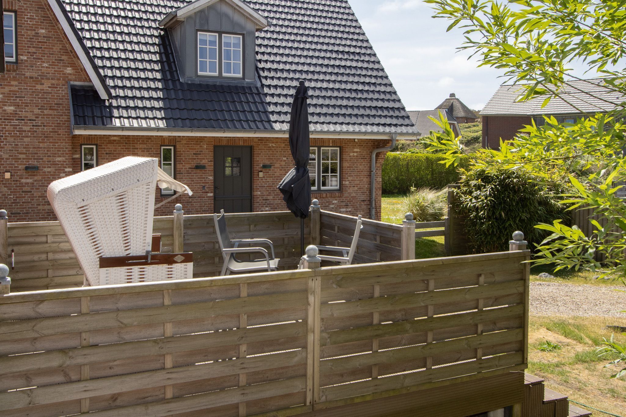 A brick house with a dark roof, a chimney, and a fenced backyard with outdoor furniture.
