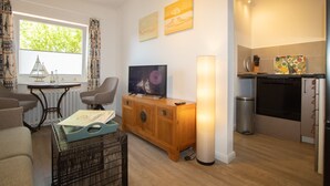 Un espacio habitable compacto con televisor, mueble de madera y una pequeña mesa de comedor.