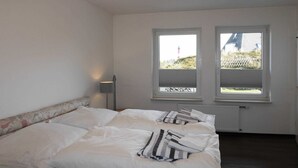 Une chambre avec un grand lit, deux fenêtres, un radiateur et une lampe.