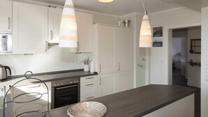 Une cuisine moderne avec des meubles blancs, un plan de travail foncé et deux lampes suspendues.