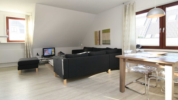 A modern living room with a black sofa, a wooden dining table, and a clear glass bar stool. - House Schössler apartment 2 (Hörnum (Sylt))