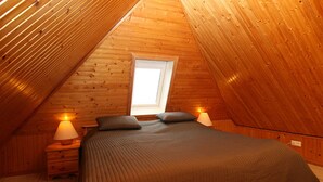 A cozy attic bedroom with a sloped ceiling, a large window, a bed with pillows, and bedside lamps. - House Schössler apartment 2 (Hörnum (Sylt))