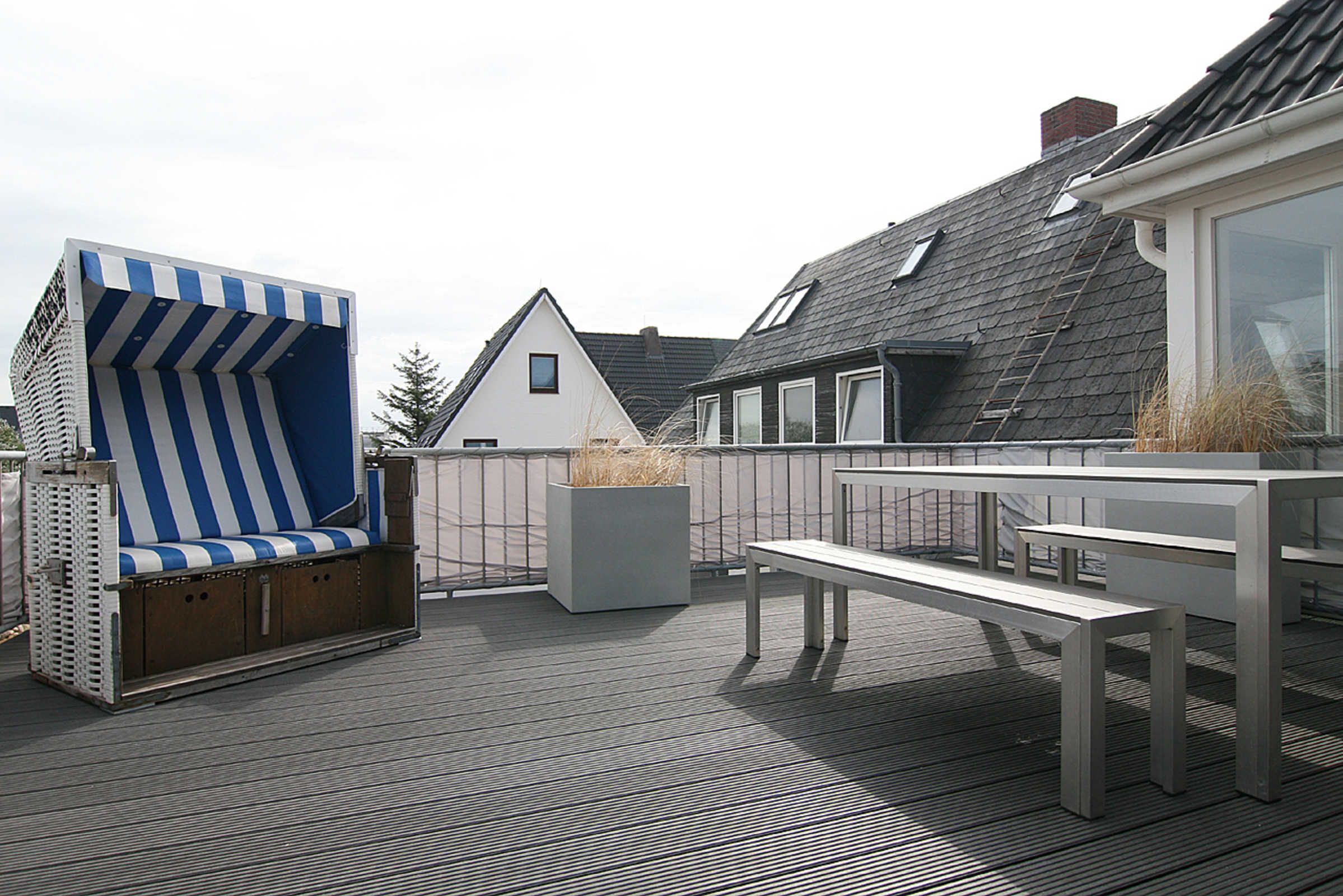 A rooftop deck with a blue and white striped chair, a white bench, and a planter with dried plants.