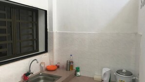 A small kitchen with a sink, a window with a metal grill, white tiled walls, and a white electric kettle. - B&L Islanders Inn - Hostel (George Town)