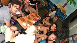 A group of people seated around a table with food, in a room with a mural of a beach scene. - B&L Islanders Inn - Hostel (George Town)
