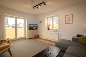 A modern living room with a sofa, a coffee table, a TV, and a window with blinds.