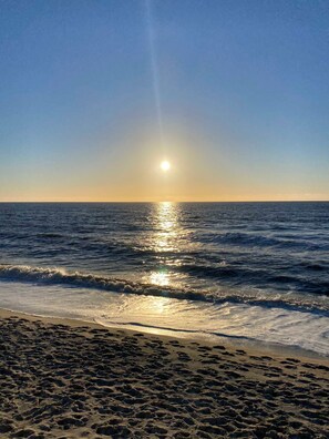 Une plage où l’on voit des empreintes de pas menant à l’eau, des vagues et un ciel dégagé.