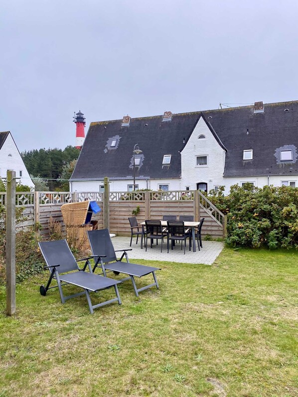 A patio area with outdoor furniture, a wooden fence, and a view of a white building with a red and white lighthouse in the background.
