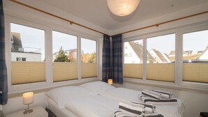 Een slaapkamer met een groot bed, een nachtkastje met een lamp en een raam met jaloezieën.