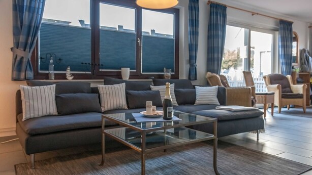Een moderne woonkamer met een donkergrijze modulaire bank, een glazen salontafel en een stadszicht door grote ramen.