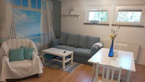 Ein Wohnzimmer mit grauem Sofa, weißem Couchtisch, weißem Sessel und einem weißen Tisch mit einer Vase.