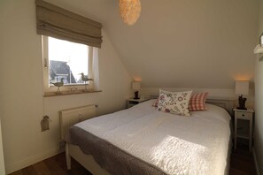 A bedroom with a large bed, a window with a view, a radiator, and bedside lamps. - Südspitze 01, Germany (Hörnum (Sylt))