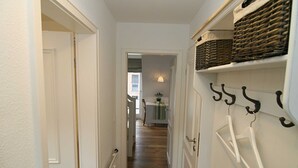 Ein schmaler Gang mit weißen Wänden und Holzboden, der zu einem Zimmer mit einem Bett und einem Fenster führt.