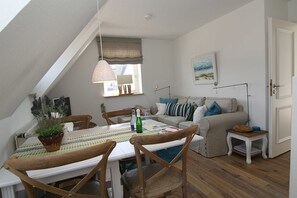 A cozy, well-lit room with a dining table, chairs, a sofa, and a small side table. - Südspitze 01, Germany (Hörnum (Sylt))