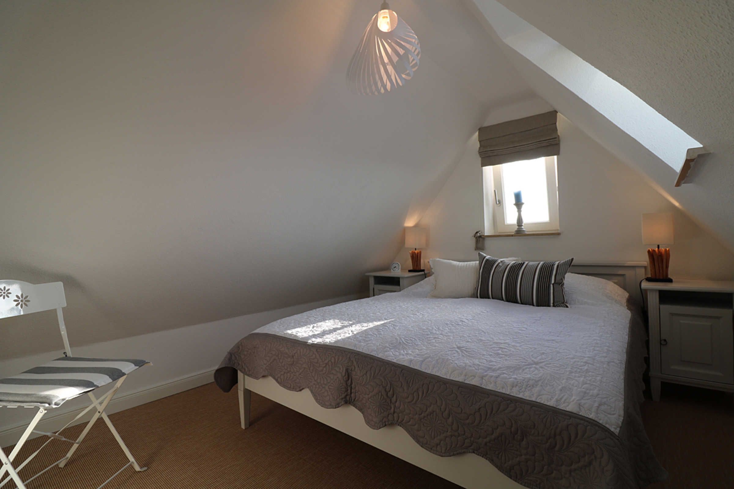 A bedroom with a bed, nightstands, a window, and a chair.
