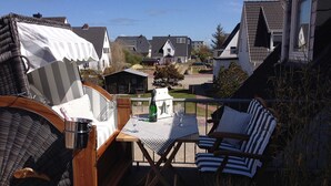 Eine Terrasse mit Gartenmöbeln, einem Tisch mit Flasche und Gläsern sowie Blick auf Häuser im Hintergrund.