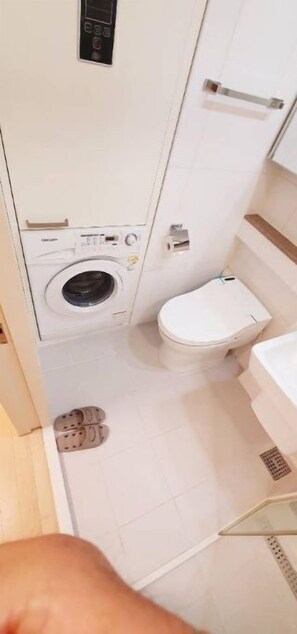 Compact bathroom with washing machine and toilet, featuring a simple layout and white tiles.
