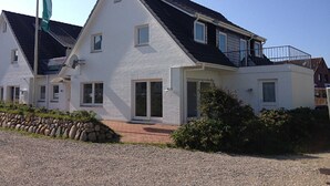 Une maison à deux étages avec un toit en pente, un balcon à l’étage supérieur et une allée gravillonnée.