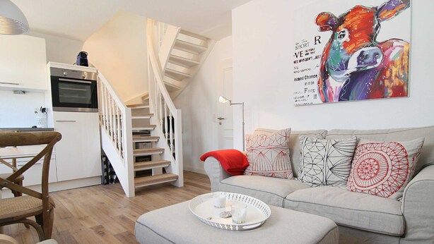 Un salon avec un canapé, une table basse ornée de bougies, un escalier et un coin cuisine.