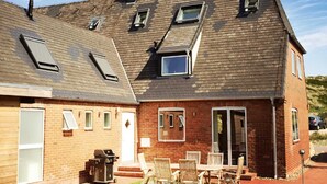 A two-story house with a sloped roof, multiple skylights, a brick exterior, and a patio with outdoor furniture. - Sylt Hüüs, Germany (Hörnum (Sylt))