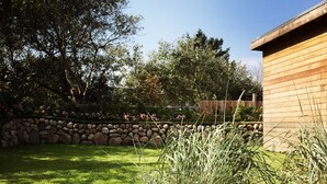 A garden with a stone wall, a wooden building, and a grassy lawn. - Sylt Hüüs, Germany (Hörnum (Sylt))