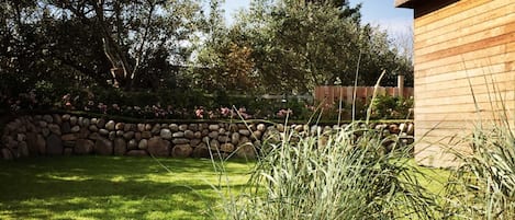 A garden with a stone wall, a wooden building, and a grassy lawn.