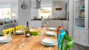A modern kitchen with a dining table set for six, surrounded by white cabinetry and a view of the outdoors. - Sylt Hüüs, Germany (Hörnum (Sylt))