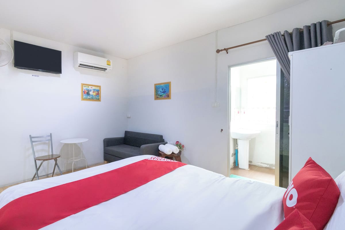 Ett hotellrum med en säng, ett skrivbord, en stol, en soffa, en tv och ett fönster med gardiner.