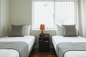 Un dormitorio con dos camas, una mesita de noche con lámpara y una ventana con persianas.