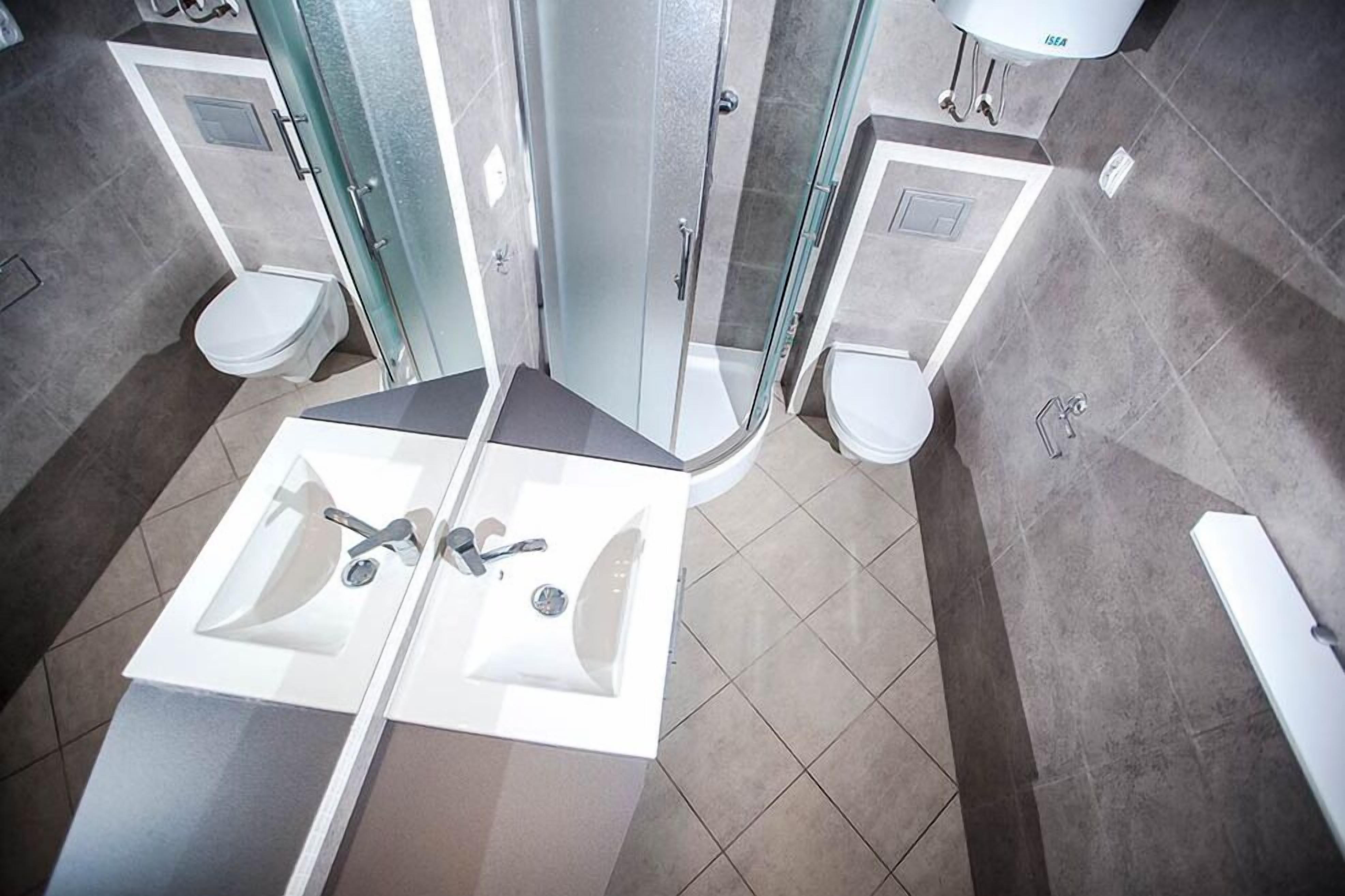 Een moderne badkamer met twee wastafels, een glazen douchecabine en een toilet.