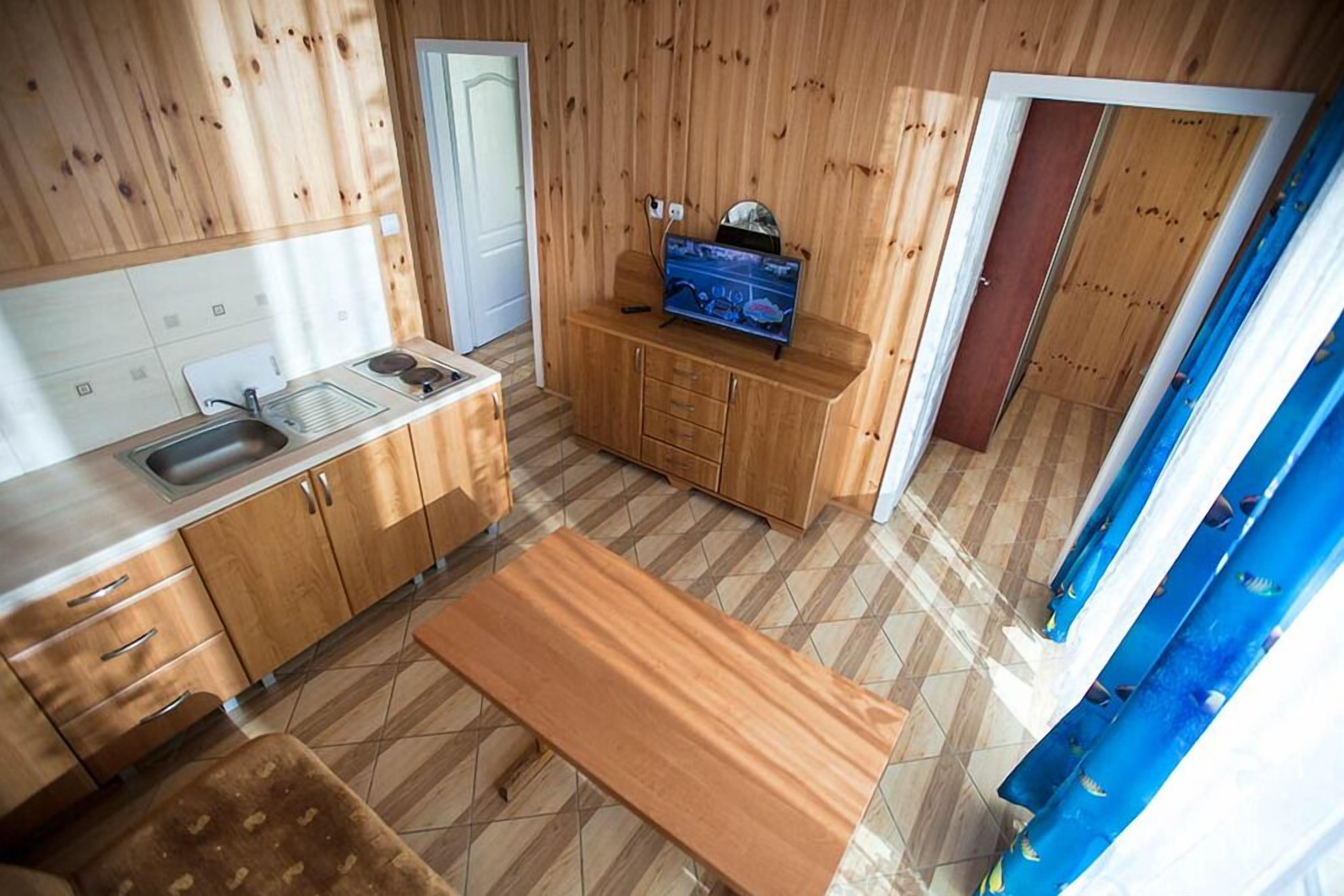 A compact kitchen with wooden cabinets, a sink, a countertop, and a bench.