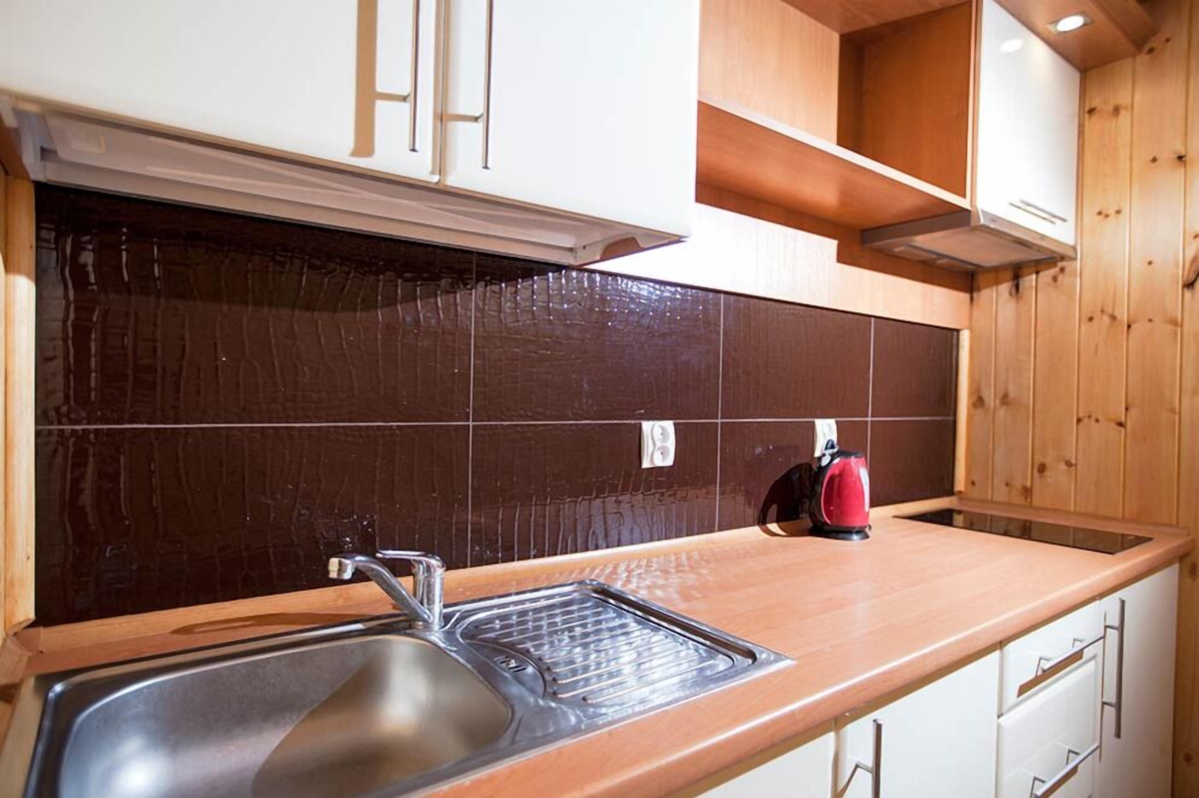 Una cocina con un lavamanos de acero inoxidable, encimera de madera y una tetera roja.