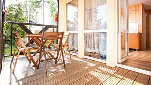Un terrazzo in legno con tavolo e sedie, ampie porte scorrevoli in vetro e vista sul verde.
