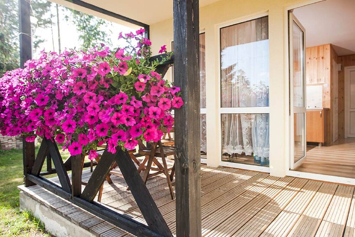 A wooden deck with a flower planter, a sliding glass door leading to a room, and a view of a forested area.