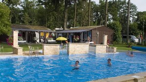 Una piscina con bordi in pietra, una zona relax coperta e un piccolo edificio con tetto.