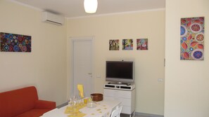 A living room with a sofa, a dining table with wine glasses, a TV, and decorative wall art.