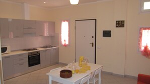 Een praktische keuken met moderne apparatuur, een eetgedeelte met een tafel voor twee en een deur met een klein raam.