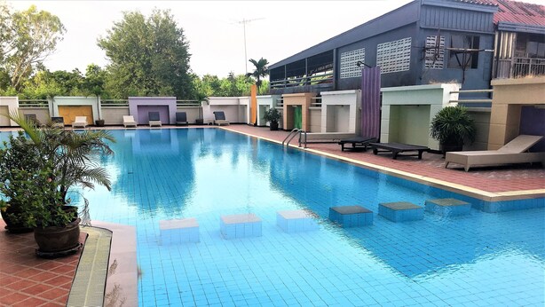 A swimming pool with tiled steps leading into the water, surrounded by lounge chairs and potted plants. - High Floor Apartment at Angket (Pattaya)