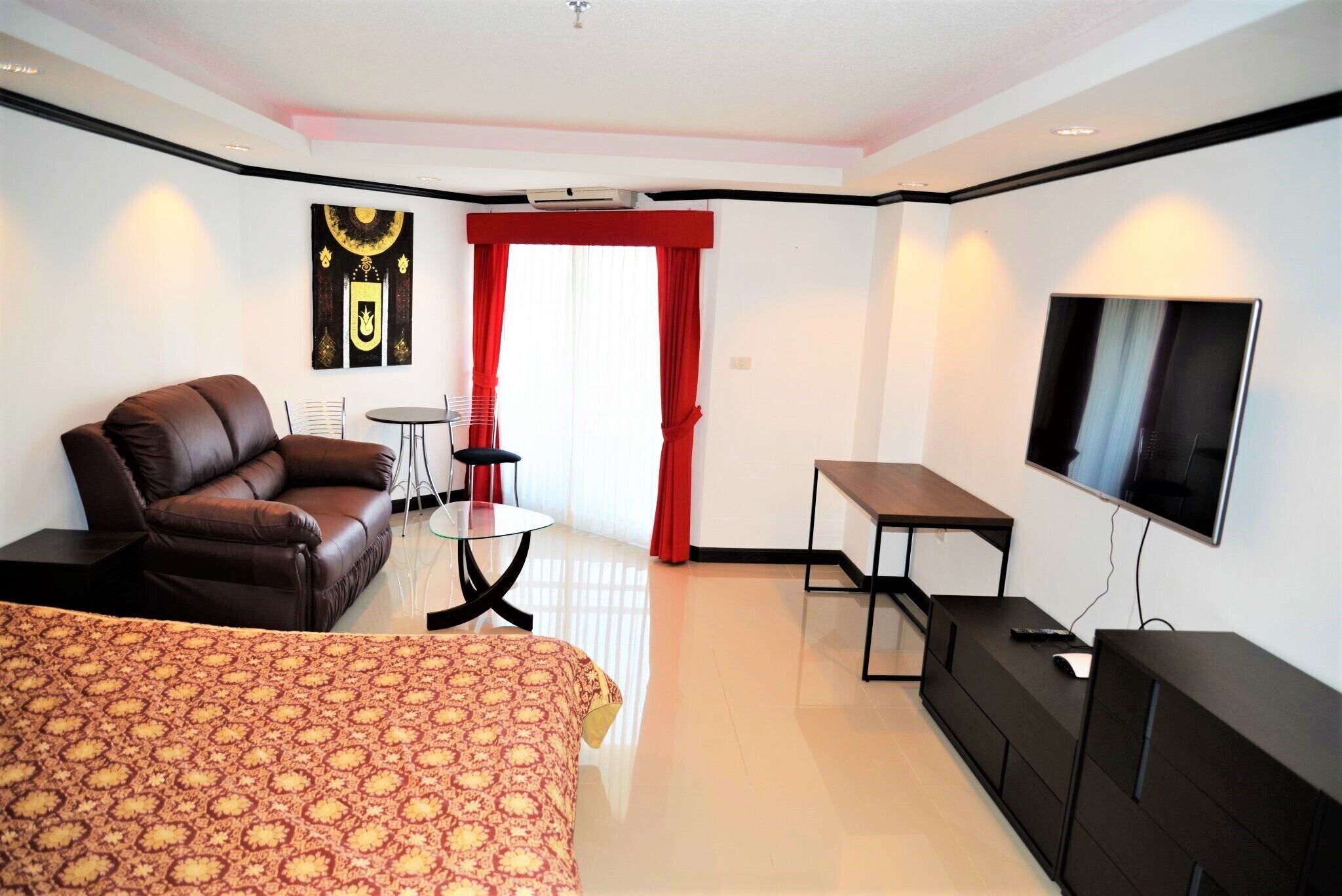 Une chambre d’hôtel moderne avec un canapé en cuir marron, une table en verre, un téléviseur et une couvre-lit à motifs.