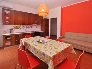 Une cuisine de taille réduite avec des meubles en bois, une table à manger recouverte d’une nappe à motifs floraux et un canapé rouge.
