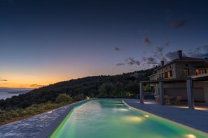 A swimming pool with a view of a hillside and a building in the background. - Gems of Pinakates (South Pelion)