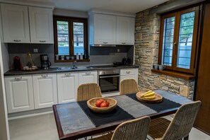 A modern kitchen with white cabinets, a stone accent wall, and a dining area with a table set for four. - Gems of Pinakates (South Pelion)